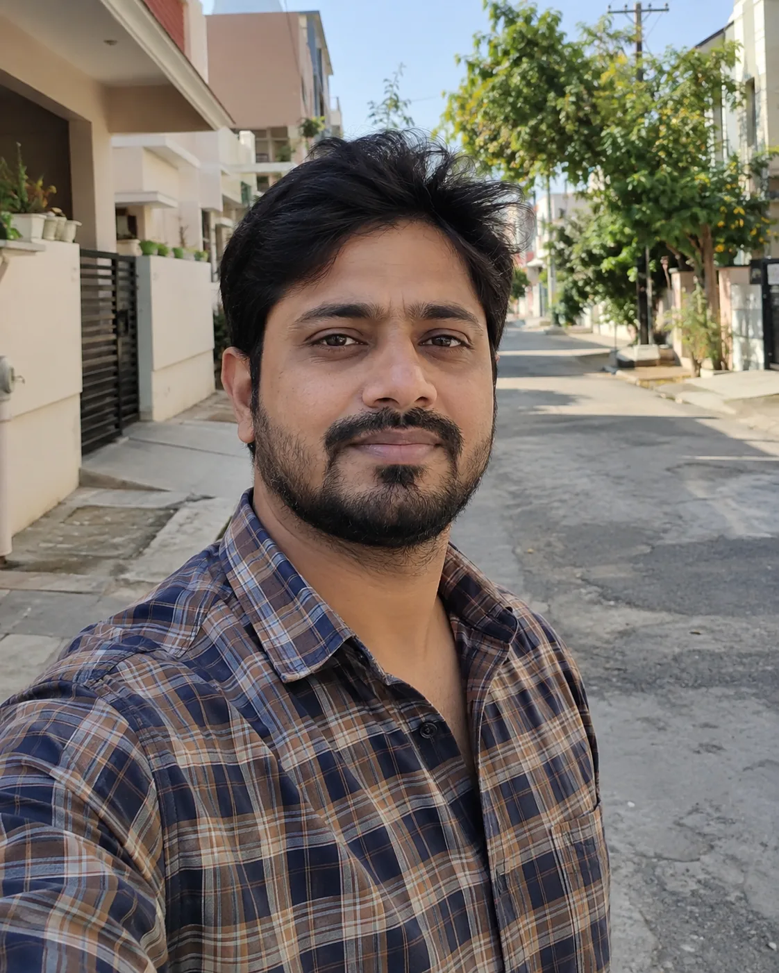 Bearded man in a brown and navy plaid shirt, on a street.