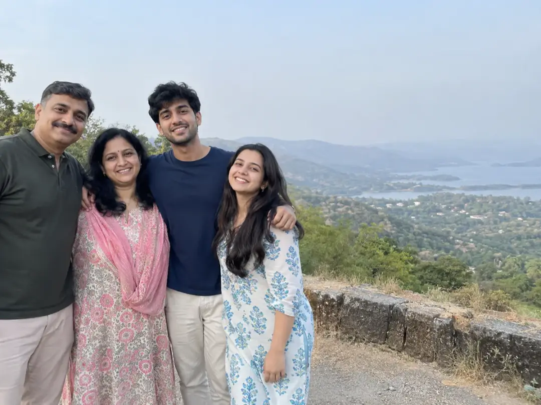 Family of four at an outdoor viewpoint: father in a dark-green polo, mother in pink floral, son in a navy tee, daughter in white and blue floral.