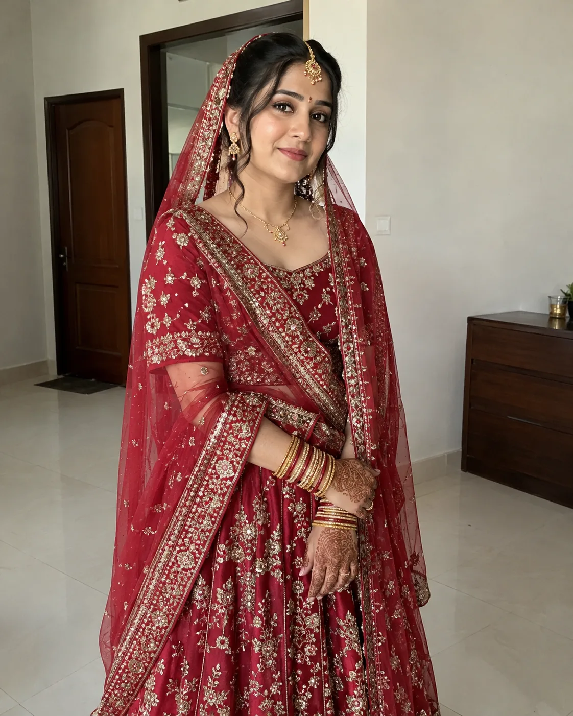 Woman in a red bridal lehenga with gold jewellery, a maang tikka and hennaed hands.